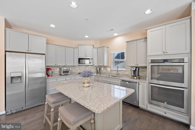 kitchen with a kitchen island, appliances with stainless steel finishes, a breakfast bar, sink, and light stone countertops