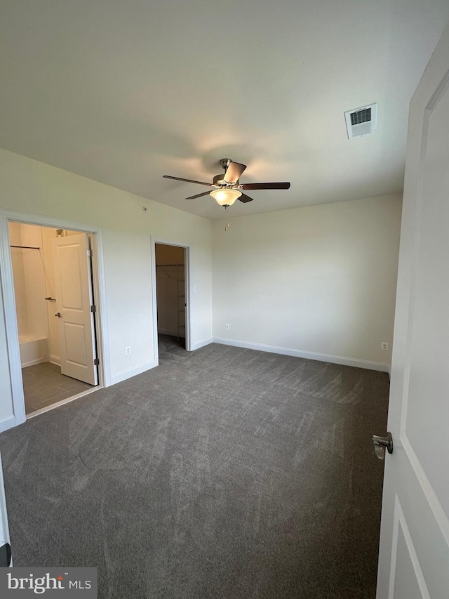 unfurnished bedroom with ceiling fan, dark carpet, and a walk in closet