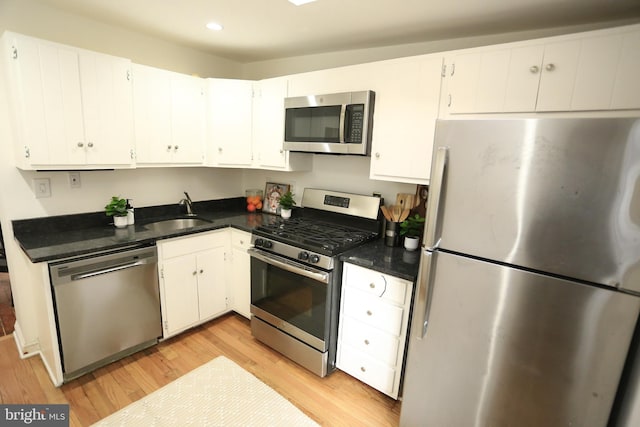 kitchen with sink, dark stone countertops, white cabinets, stainless steel appliances, and light hardwood / wood-style flooring