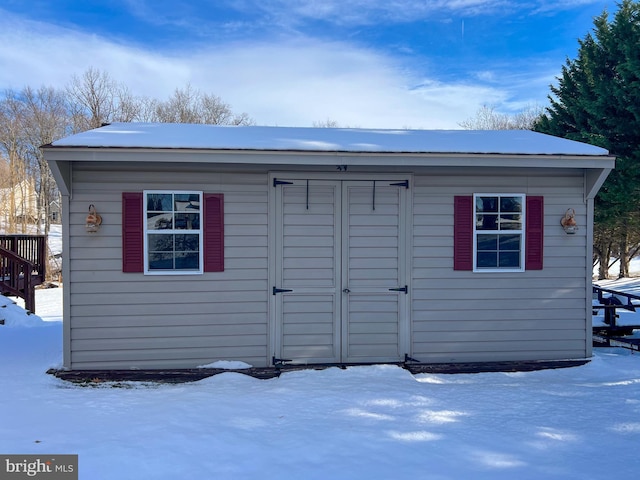 snow covered structure featuring an outbuilding and a shed