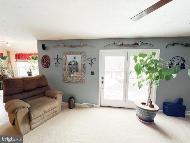 living room featuring a textured ceiling, carpet flooring, visible vents, and baseboards