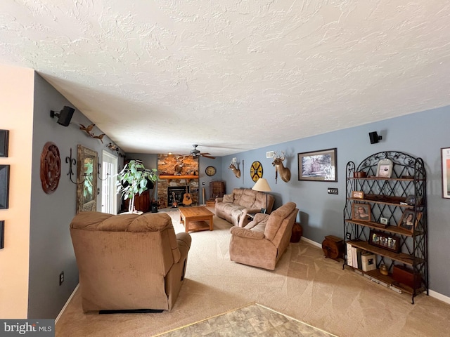 living area with a ceiling fan, light carpet, a stone fireplace, a textured ceiling, and baseboards