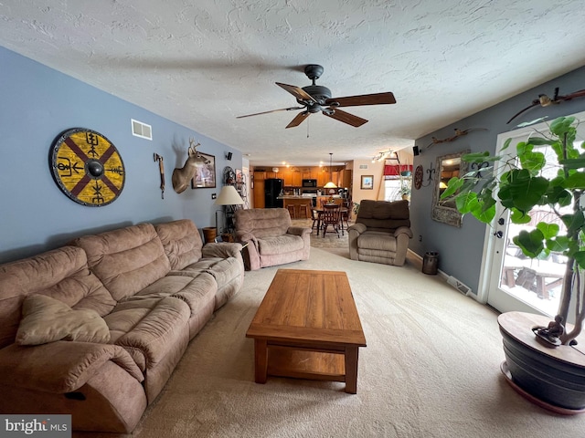 living area featuring a textured ceiling, ceiling fan, light carpet, and visible vents