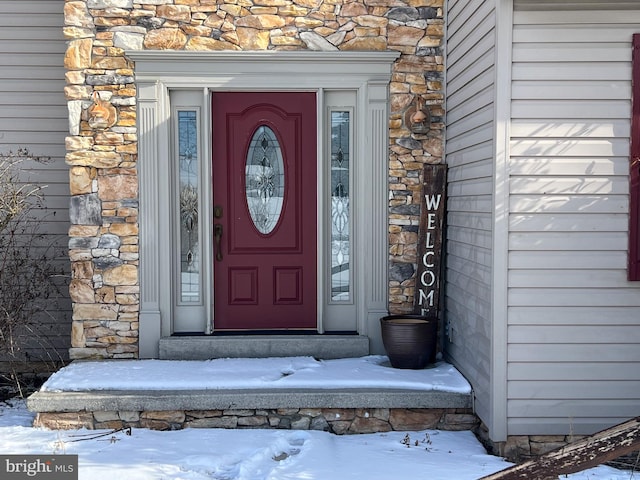 snow covered property entrance with stone siding