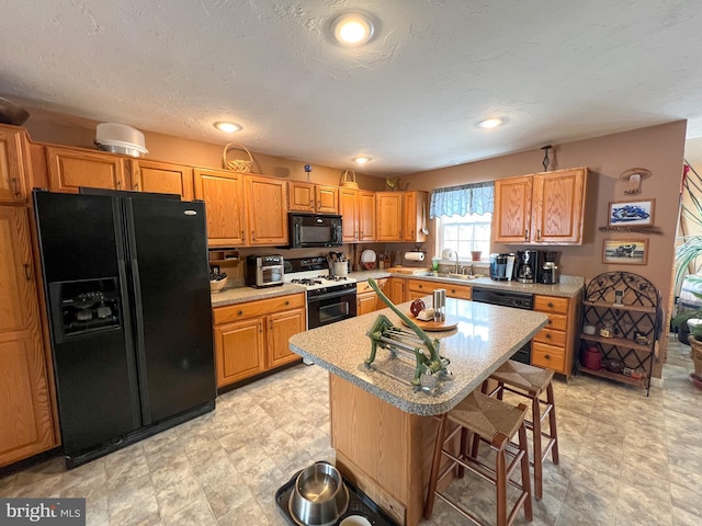 kitchen featuring a breakfast bar, light countertops, a sink, and black appliances