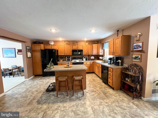 kitchen featuring a kitchen island, light countertops, black appliances, a kitchen bar, and a sink