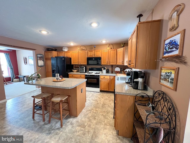 kitchen featuring a breakfast bar, a center island, light countertops, a sink, and black appliances