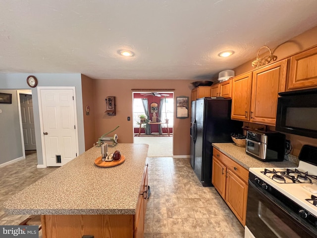 kitchen with baseboards, brown cabinetry, a center island, light countertops, and black appliances