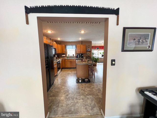 kitchen featuring a center island, baseboards, brown cabinets, black appliances, and a kitchen bar