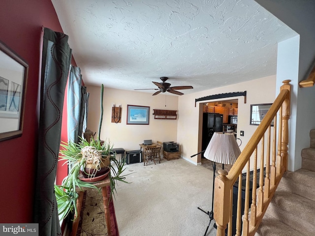 living area featuring a ceiling fan, carpet, a textured ceiling, and stairs