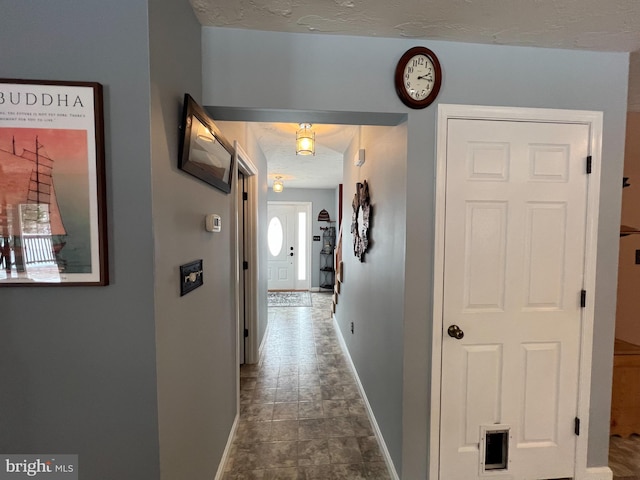 corridor featuring a textured ceiling and baseboards