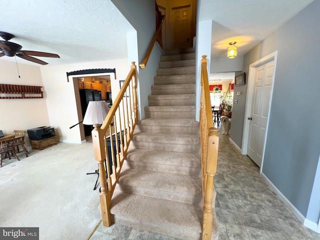 staircase with a ceiling fan, a textured ceiling, and baseboards