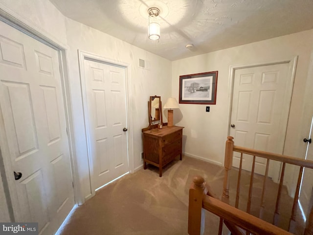 interior space with light carpet, an upstairs landing, visible vents, and baseboards