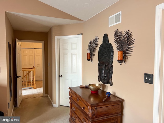 corridor featuring light colored carpet, visible vents, vaulted ceiling, and baseboards