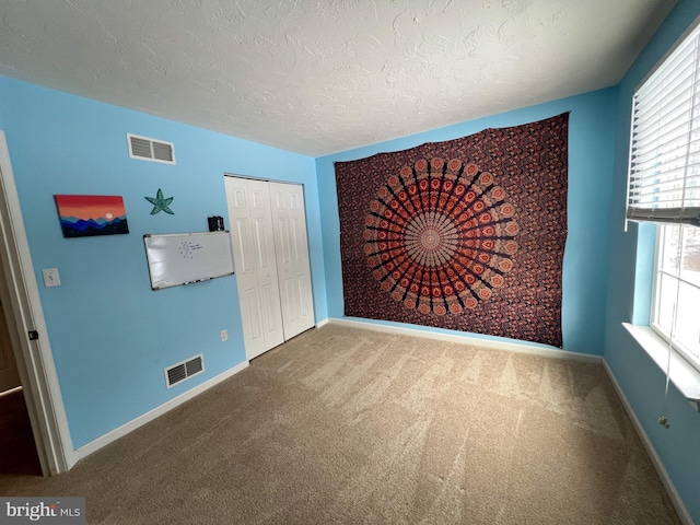 carpeted empty room featuring a textured ceiling, visible vents, and baseboards