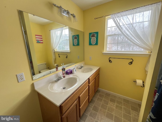 bathroom with toilet, double vanity, baseboards, and a sink