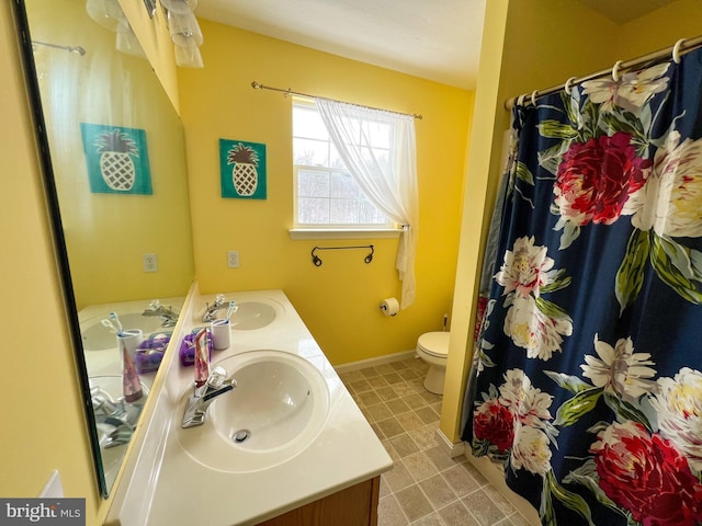 bathroom featuring double vanity, a sink, toilet, and baseboards