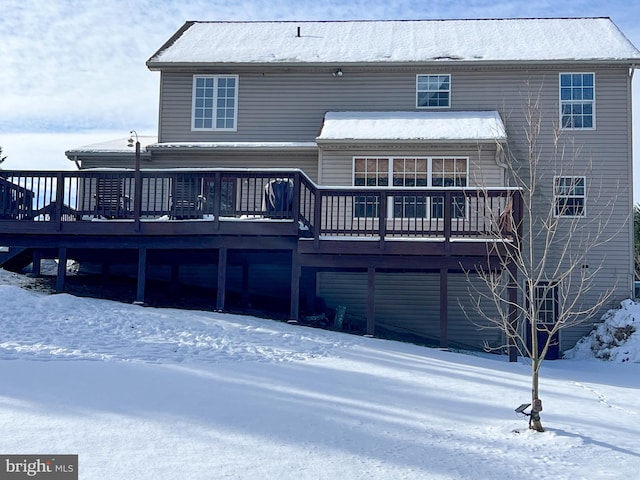 snow covered back of property with a wooden deck