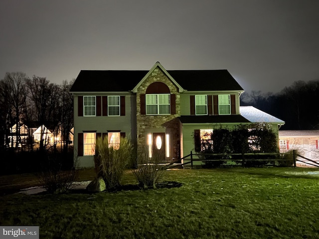 colonial-style house with a yard and stone siding