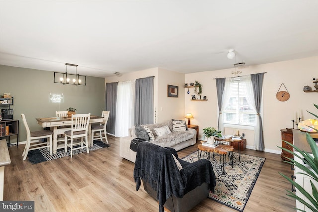 living room featuring visible vents, baseboards, light wood-style floors, and a notable chandelier