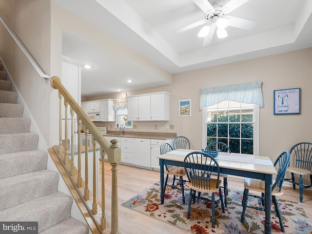 dining room featuring sink, a tray ceiling, light hardwood / wood-style flooring, and ceiling fan