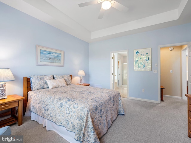 carpeted bedroom with ceiling fan, ensuite bath, and a tray ceiling