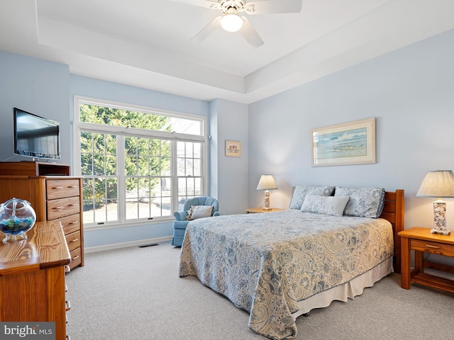 bedroom with light colored carpet, a raised ceiling, and ceiling fan