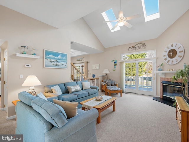 carpeted living room with ceiling fan, high vaulted ceiling, a fireplace, and a skylight