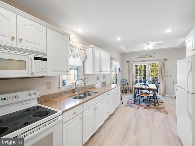 kitchen featuring sink, white cabinetry, light hardwood / wood-style flooring, a tray ceiling, and white appliances