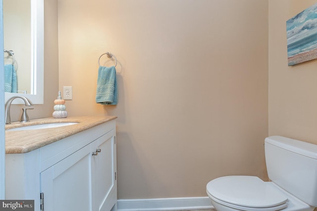 half bath featuring baseboards, vanity, and toilet