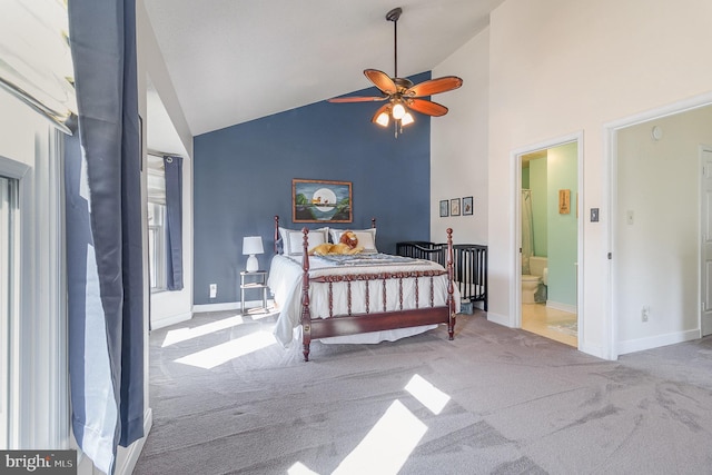 bedroom featuring light colored carpet, ceiling fan, ensuite bath, high vaulted ceiling, and baseboards