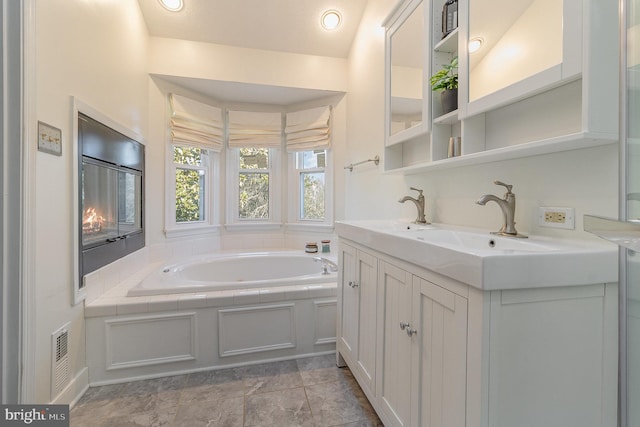 full bath featuring visible vents, double vanity, a sink, and a bath