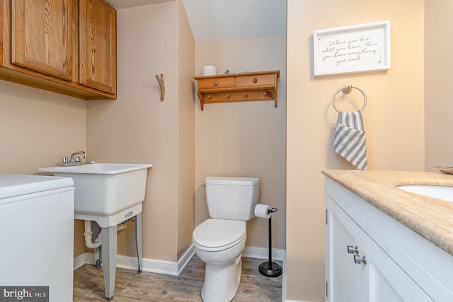 bathroom with washer / dryer, baseboards, toilet, wood finished floors, and vanity