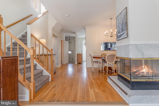 entrance foyer featuring a tiled fireplace, wood finished floors, stairs, crown molding, and a chandelier