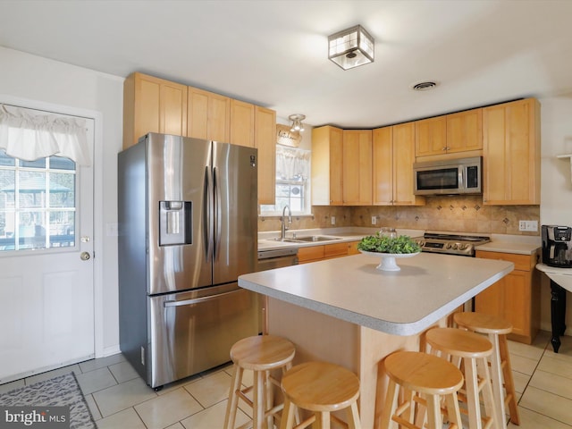 kitchen with sink, appliances with stainless steel finishes, a kitchen breakfast bar, a kitchen island, and decorative backsplash