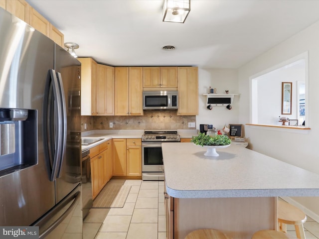 kitchen with a kitchen island, light brown cabinetry, a kitchen bar, light tile patterned floors, and stainless steel appliances