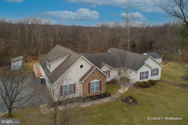 view of front of property featuring stone siding, a wooded view, and a front lawn