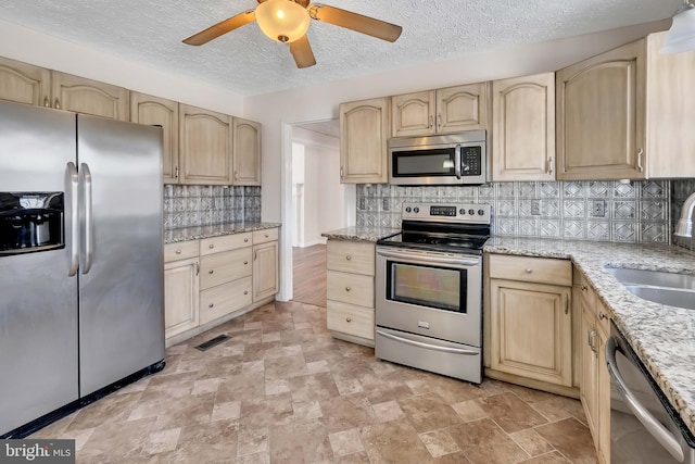 kitchen featuring decorative backsplash, light stone countertops, stainless steel appliances, light brown cabinetry, and a sink