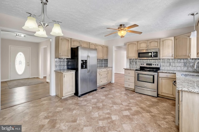 kitchen featuring light stone counters, light brown cabinets, ceiling fan with notable chandelier, stainless steel appliances, and decorative backsplash