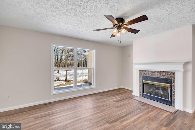 unfurnished living room with baseboards, visible vents, wood finished floors, and a glass covered fireplace