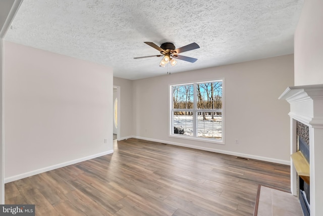 unfurnished living room with ceiling fan, wood finished floors, a fireplace with flush hearth, visible vents, and baseboards