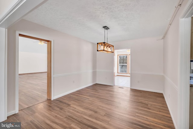 empty room featuring ceiling fan, a textured ceiling, baseboards, and wood finished floors