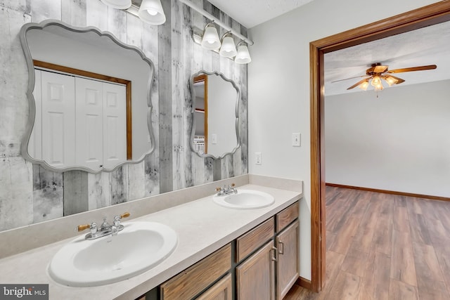 full bath with double vanity, a sink, baseboards, and wood finished floors