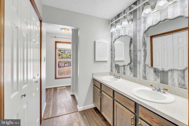 full bath with double vanity, a textured ceiling, a sink, and wood finished floors