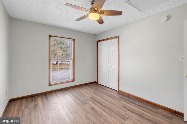 unfurnished bedroom with a closet, a textured ceiling, baseboards, and wood finished floors