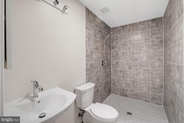 bathroom featuring visible vents, a sink, a tile shower, and toilet