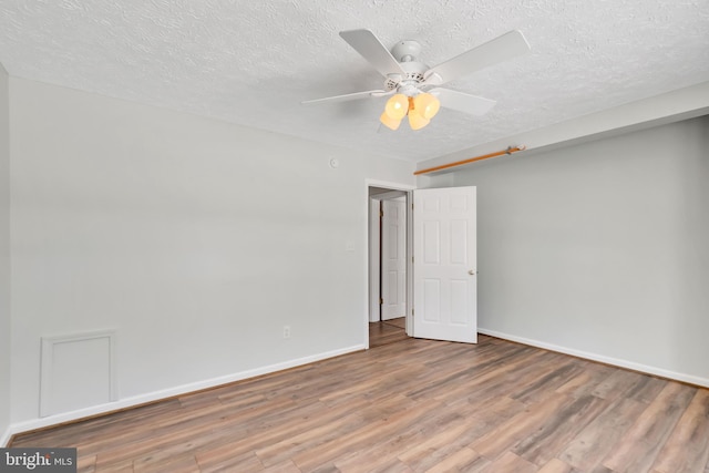 empty room with a ceiling fan, a textured ceiling, baseboards, and wood finished floors