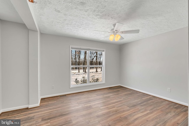 empty room with visible vents, ceiling fan, a textured ceiling, wood finished floors, and baseboards