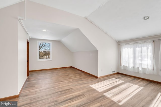 additional living space with vaulted ceiling, visible vents, light wood-style flooring, and baseboards