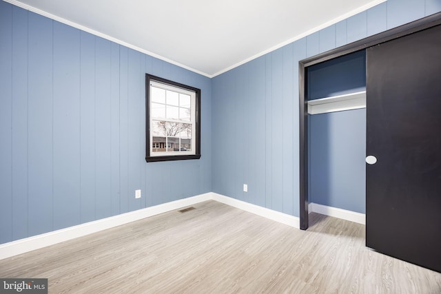 unfurnished bedroom featuring crown molding, light hardwood / wood-style floors, and a closet